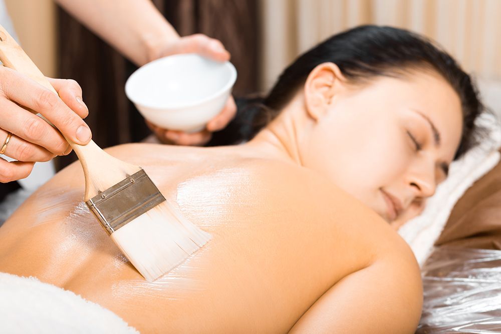 Spa therapist applying cream to a woman's back during a massage treatment