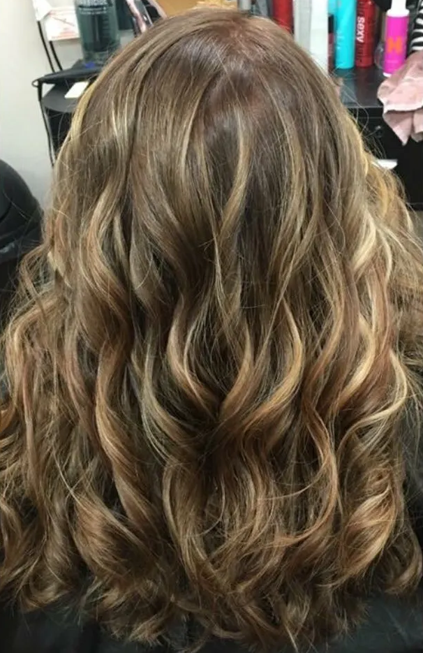 Wavy shoulder-length brown hair with blonde highlights, shown from the back in a salon chair.