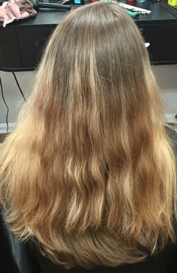 Back view of long, wavy blonde hair in a salon chair, with darker roots near the crown.