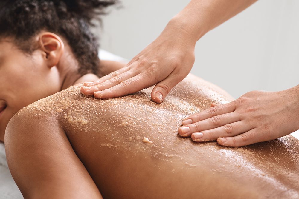 Hands massaging a person's back with exfoliating scrub in a spa setting