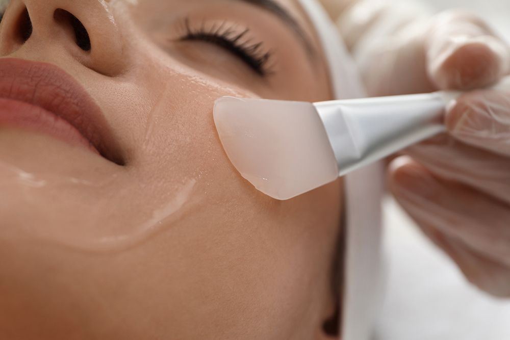 Facial skincare treatment with a cream mask being applied to a woman's cheek with a brush