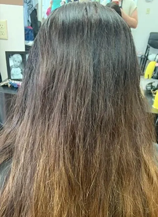 Back view of long dark brown hair with lighter ombrÃ© ends in a salon setting
