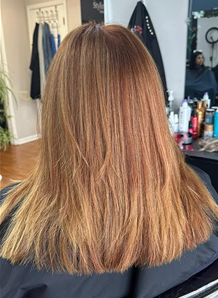 Back view of shoulder-length light brown hair with blonde highlights in a salon chair