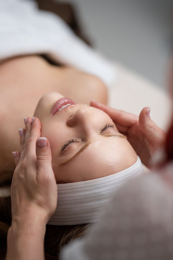 Person receiving a facial massage with eyes closed, wearing a white headband.