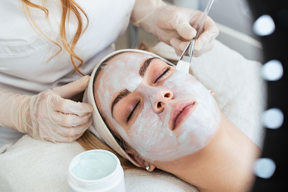 Esthetician applying a facial mask to a reclining client in a spa treatment room