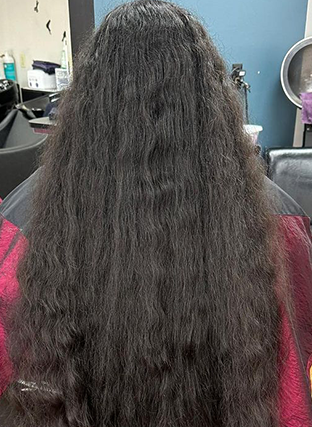 Back view of a person with long, dark, wavy hair in a salon chair