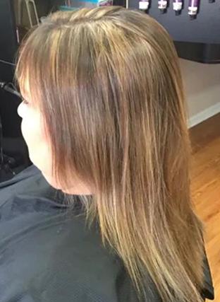 Side view of a layered brown-and-blonde haircut in a salon chair, showing highlighted hair and bangs
