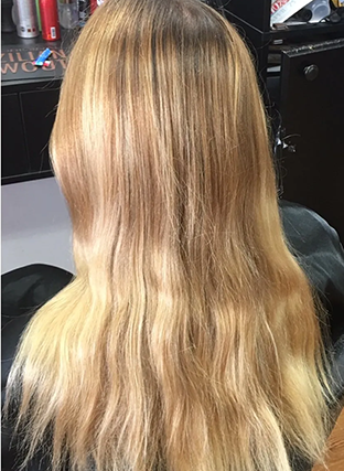 Back view of long wavy blonde hair with darker roots in a salon chair