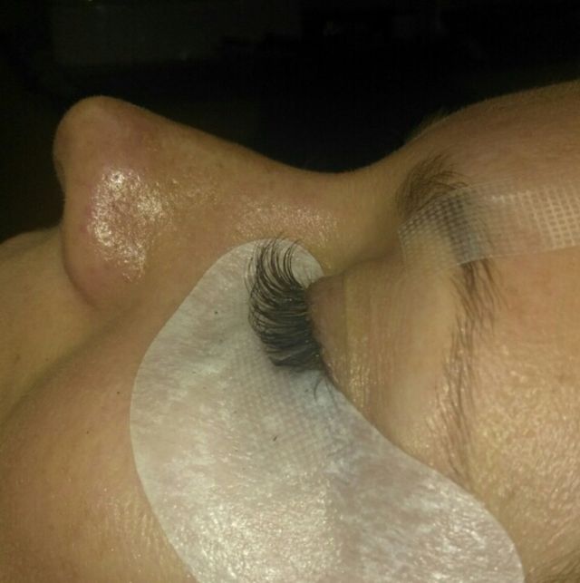 Close-up of a person's closed eye with a white under-eye eye pad applied, showing a long eyelash extension.