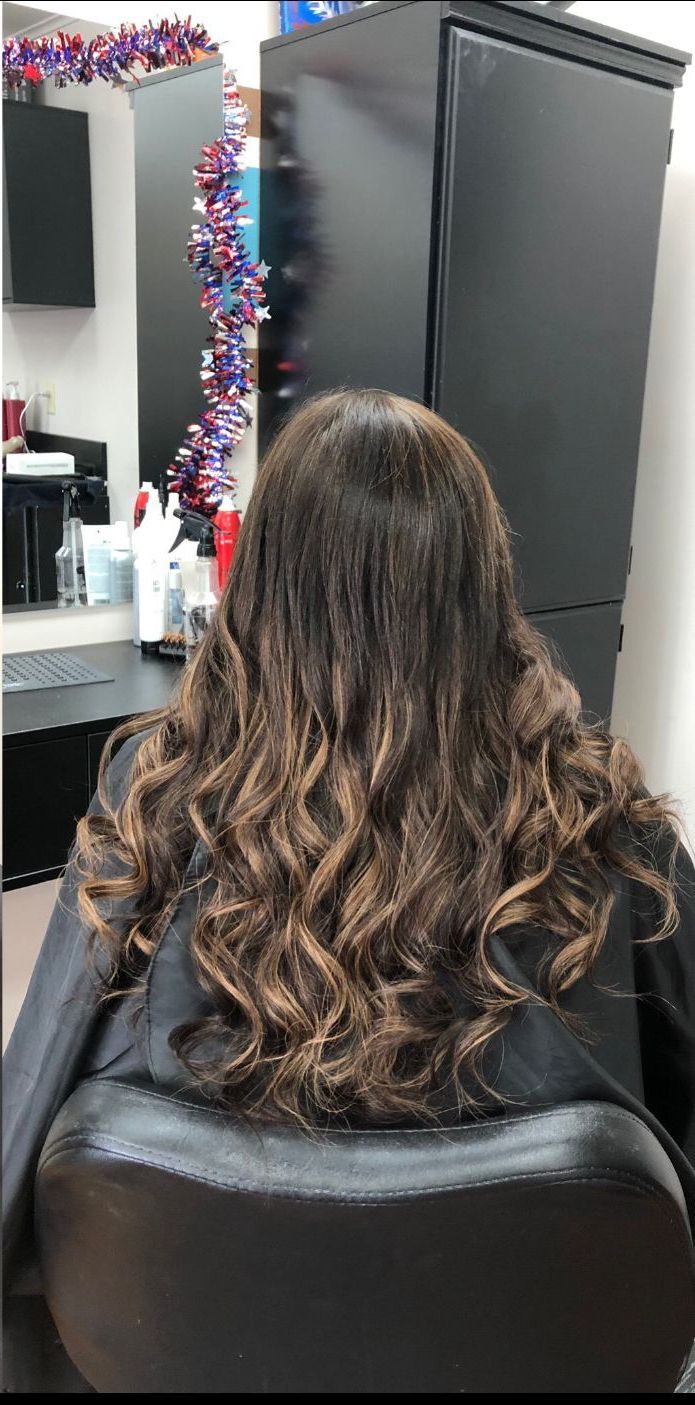 Wavy brown hair from behind in a salon chair, with a mirror and black styling station nearby