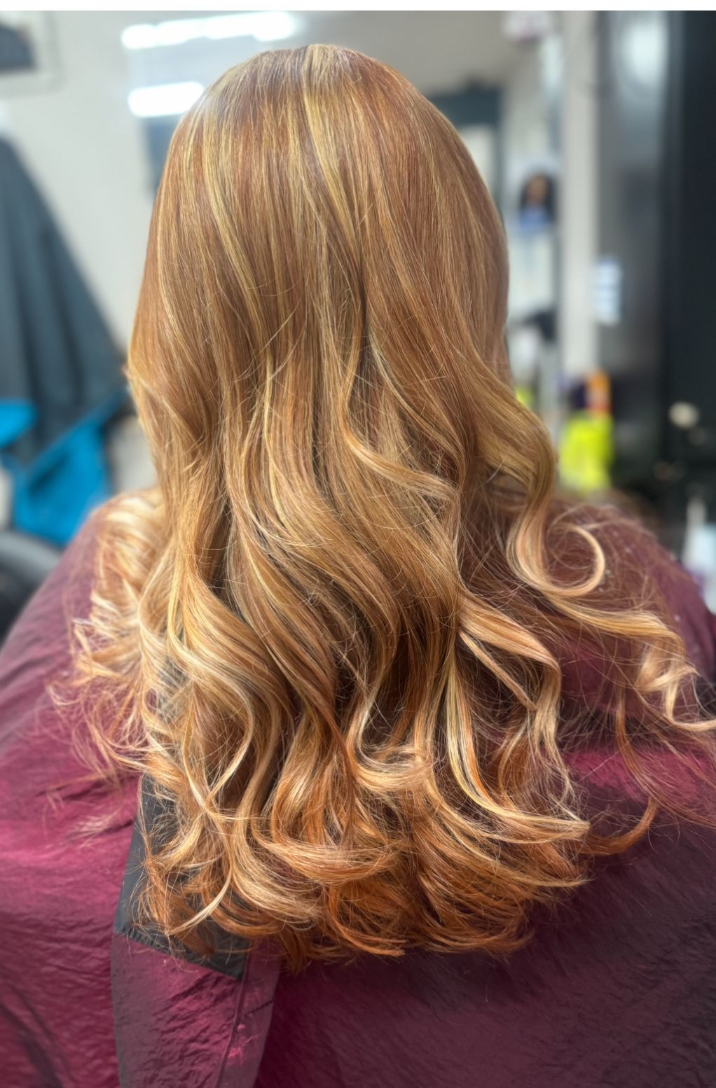 Back view of a person with long wavy blonde hair wearing a maroon top