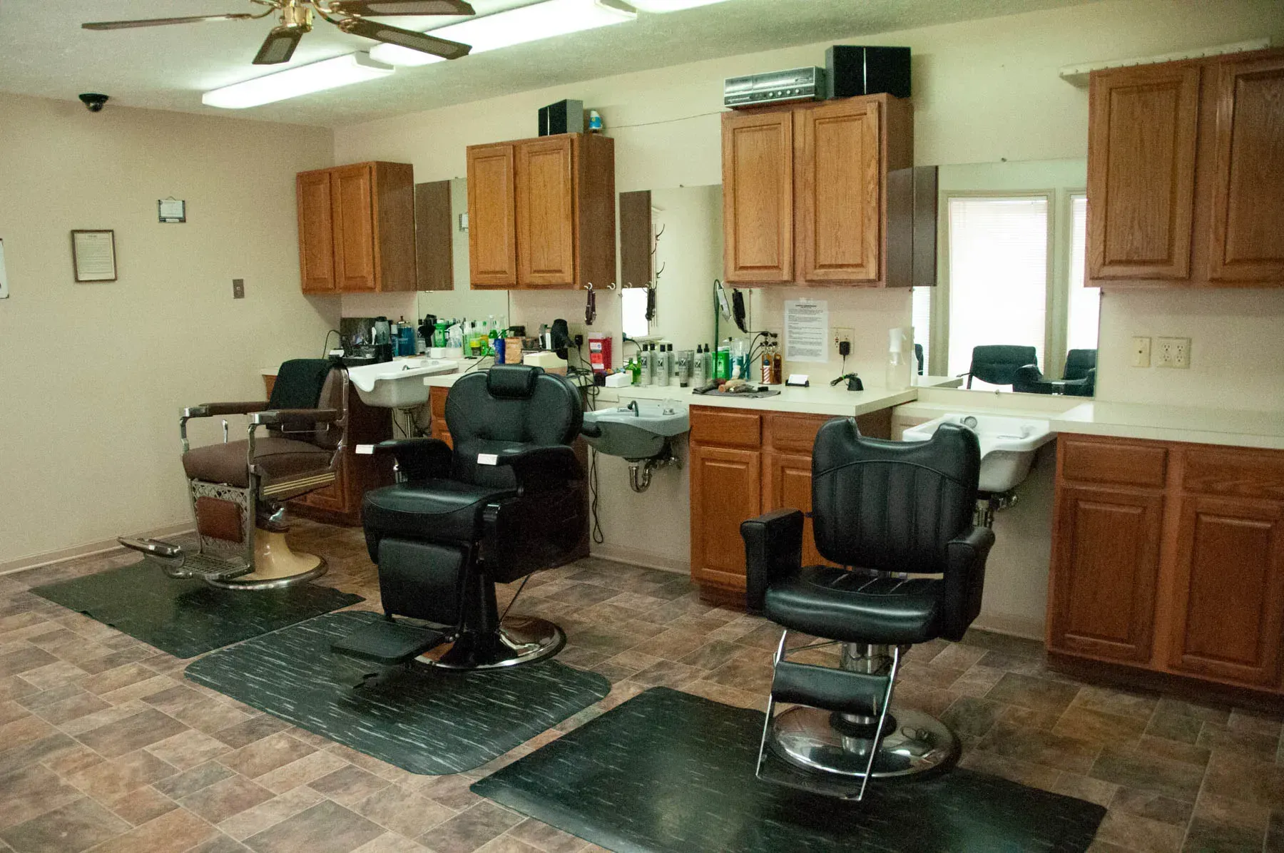 Barbershop interior with two black styling chairs, wooden cabinets, sinks, and mirrors.