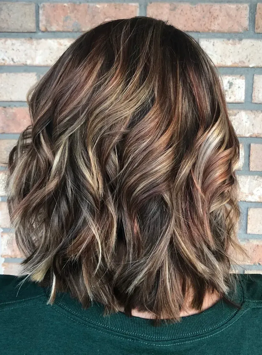 Shoulder-length wavy brown hair with blonde highlights against a brick wall