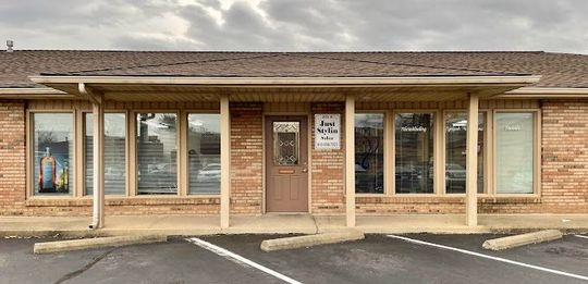 Brick storefront with glass windows, a centered door, and an empty parking lot in front