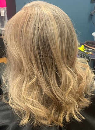 Blonde wavy shoulder-length hair with subtle highlights, viewed from behind in a salon chair