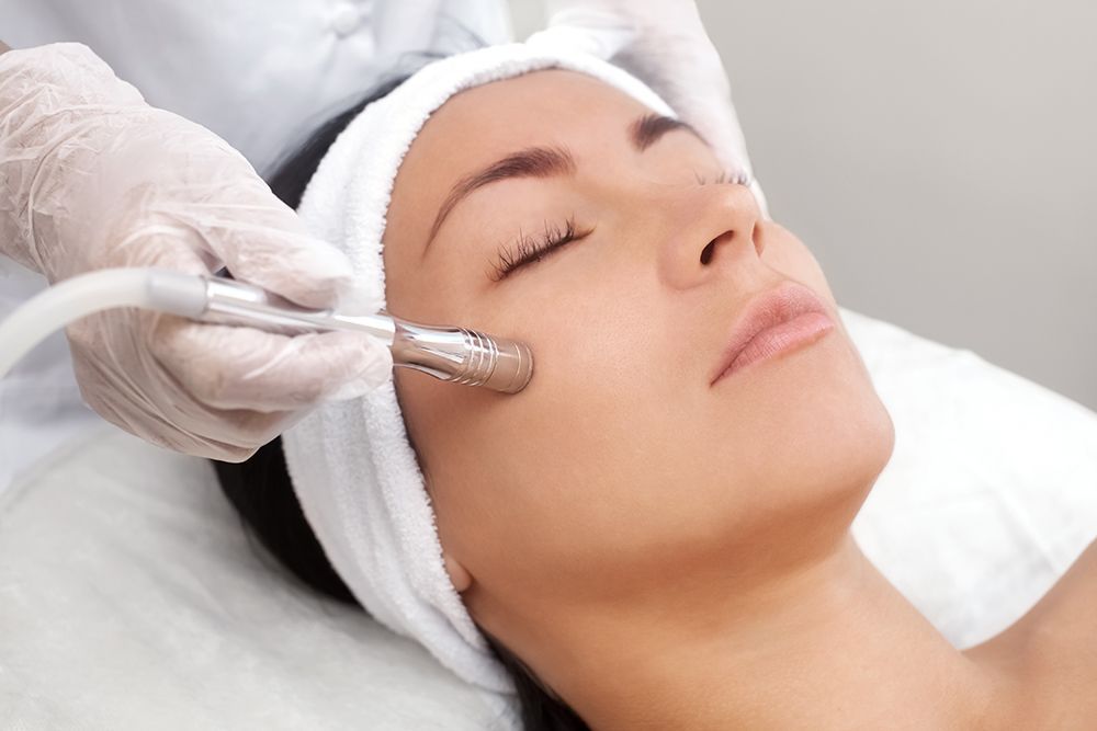 Woman receiving a facial treatment with a handheld device while lying on a spa bed