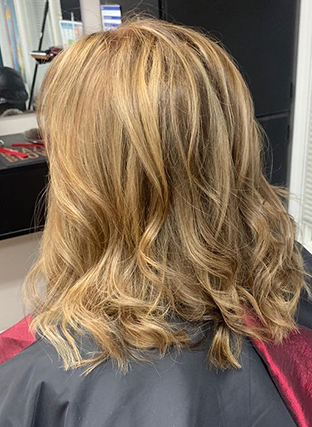 Shoulder-length wavy blonde hair with light highlights, viewed from the back in a salon chair