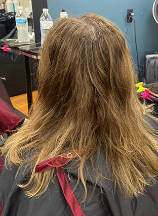 Back view of shoulder-length wavy brown hair with blonde highlights and a red ribbon in a salon chair