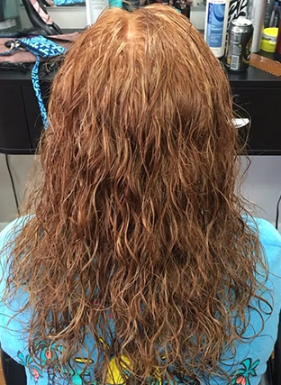 Back view of long wavy auburn hair with blonde highlights, seated in a salon chair