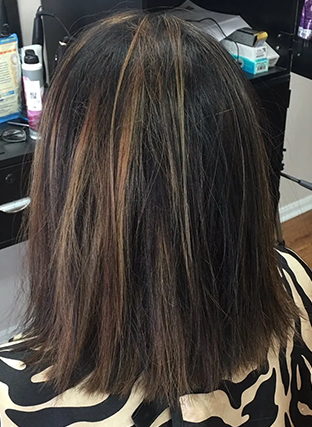 Back of head with dark hair and blonde highlights, styled in a shoulder-length cut at a salon chair