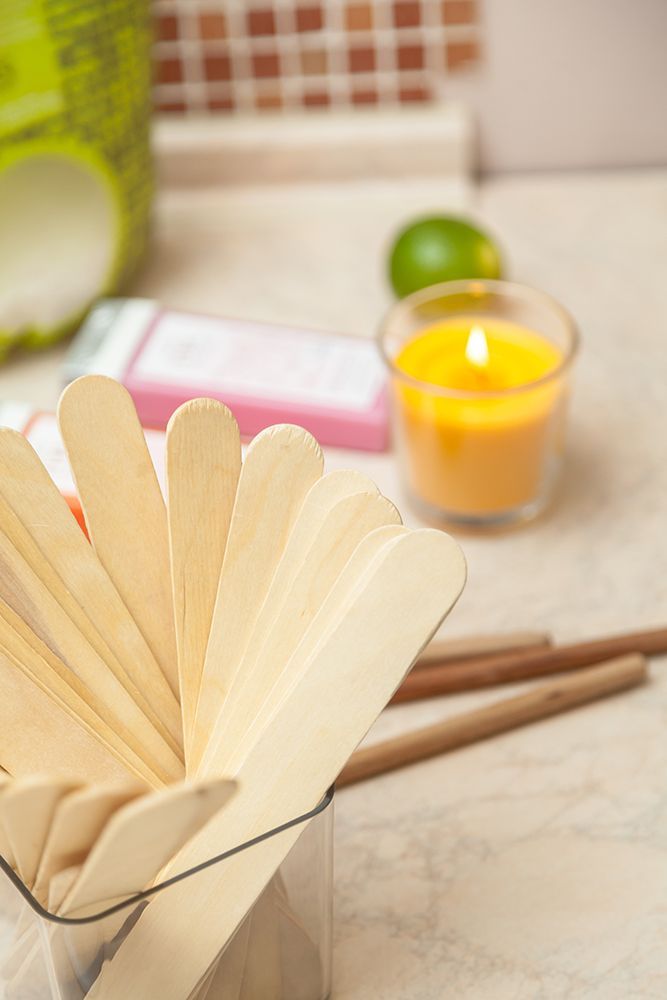 Wooden craft sticks in a glass jar beside a lit yellow candle on a table