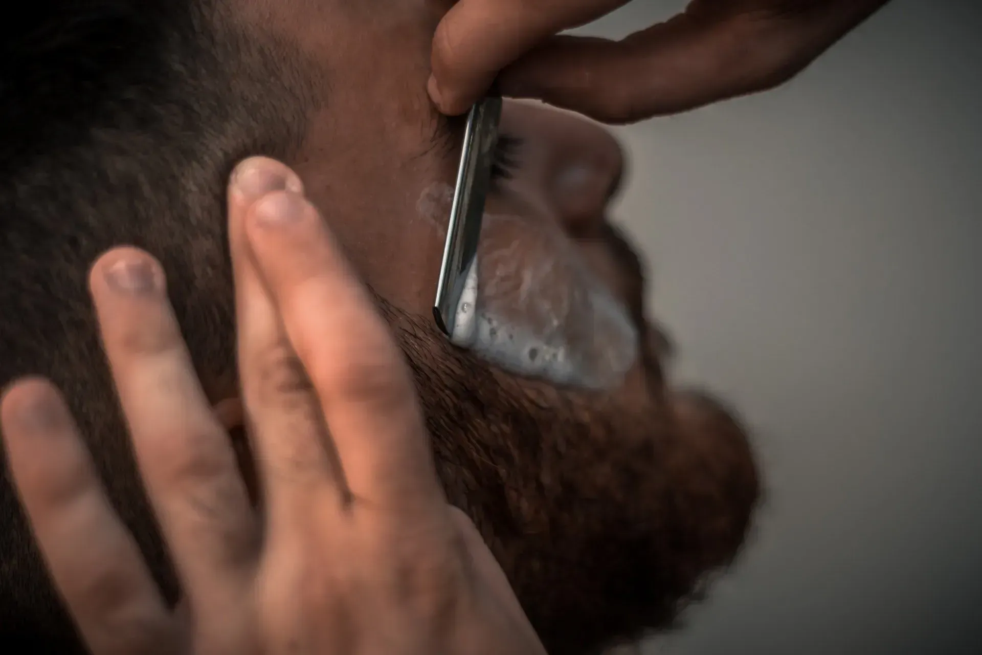 Close-up of a person trimming a beard with electric clippers while holding a phone to the ear